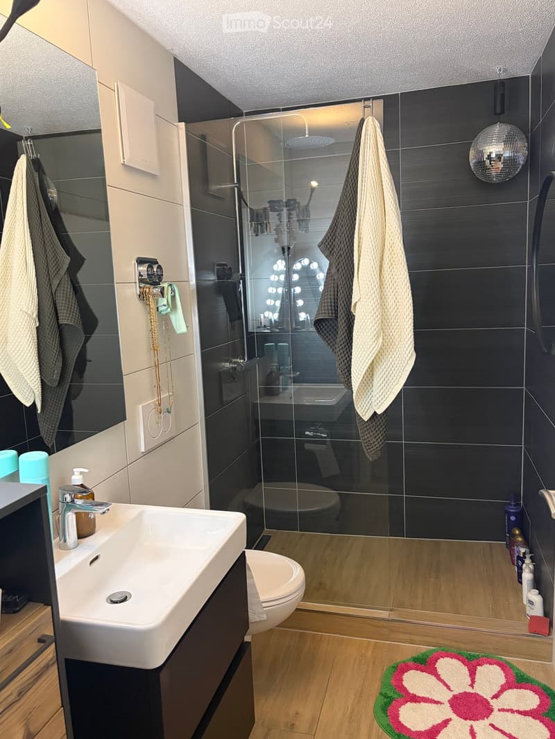 Modern bathroom with a white sink, chrome faucet, toilet, glass-enclosed shower, towels, and decorative items.