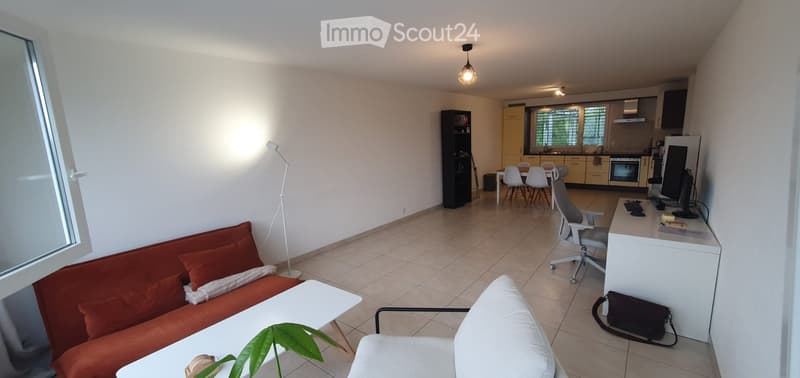 A modern, open-plan living and dining area with a red sofa, white coffee table, white dining table with chairs, a kitchen area with cabinets and appliances, and a workspace with a desk and chair.