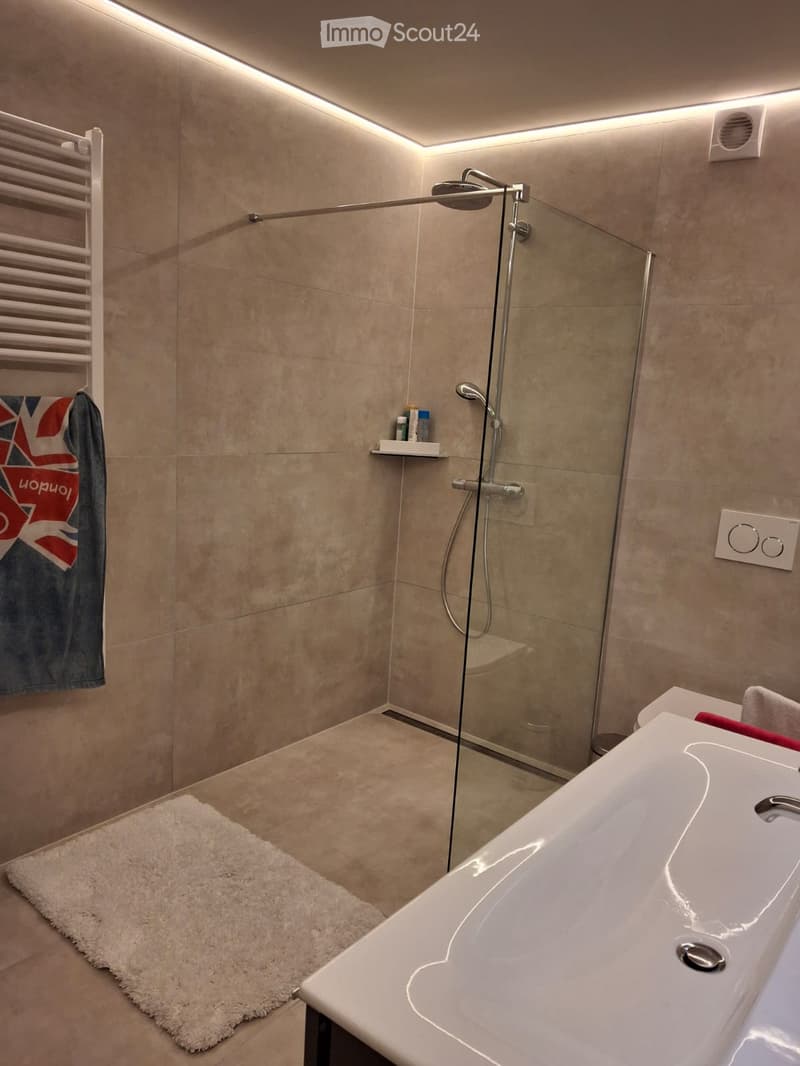 Modern bathroom with a bathtub, glass-enclosed shower, towel rack, and a small shelf holding toiletries.