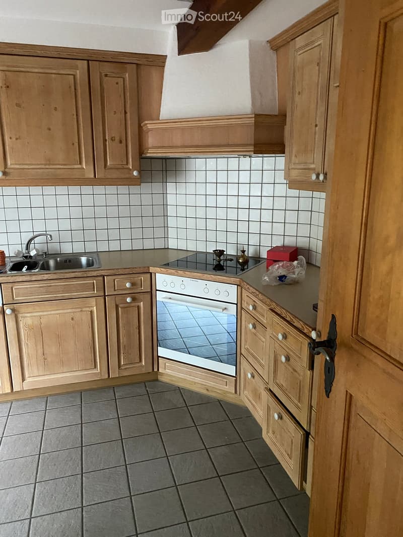 A small kitchen with light wooden cabinets, a sink, an oven, and a tiled backsplash.