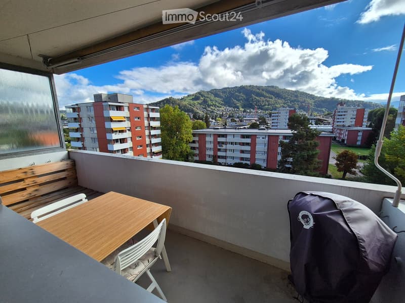 Balcony with wooden table, chairs, bench, and scenic mountain view.