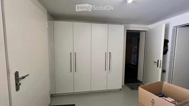 Empty room with white built-in wardrobes, grey flooring, and a partially open doorway leading to another room.