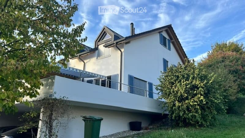 Modern two-story house with white exterior, blue shutters, and a large balcony on the first floor.