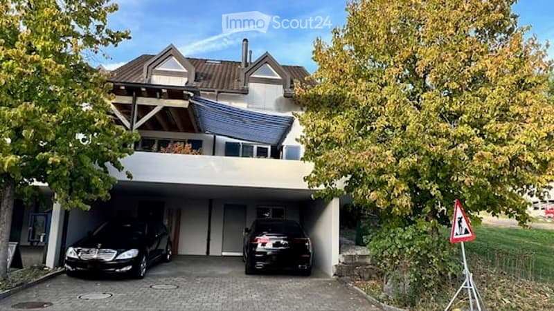 Two-story house with a garage and two parked cars, surrounded by trees.