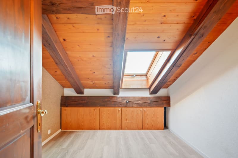 An unfurnished room with wooden ceiling beams, skylight windows, wooden cabinetry, and light wooden flooring.