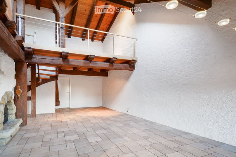 Spacious hallway with exposed wooden beams, a staircase leading to an upper level, and a stone fireplace on the left side.