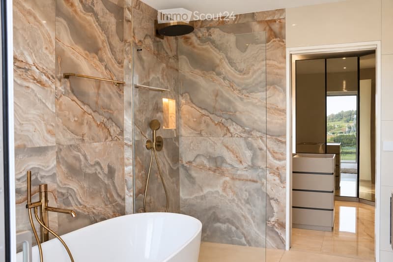 Modern bathroom with marble walls, a freestanding bathtub, gold fixtures, a glass-enclosed shower, and a mirrored vanity with storage.