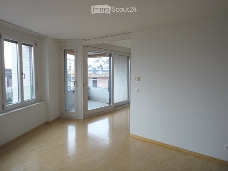 Empty room with wooden flooring, large windows, and sliding glass doors leading to a balcony.