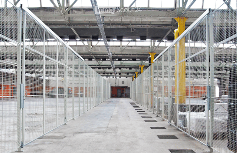 An empty industrial-style corridor with metal fencing on both sides, concrete floor, exposed metal beams, and yellow structural columns.
