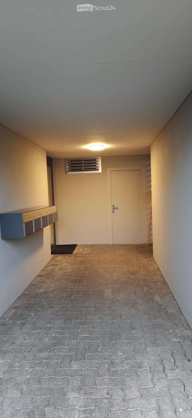 Empty hallway with tiled floor, white walls, a closed door, and a small cabinet on the left side.