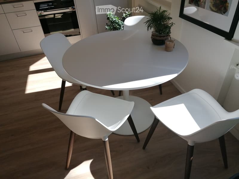 Modern white dining table with four white chairs, small potted plants, and a candle on the table.