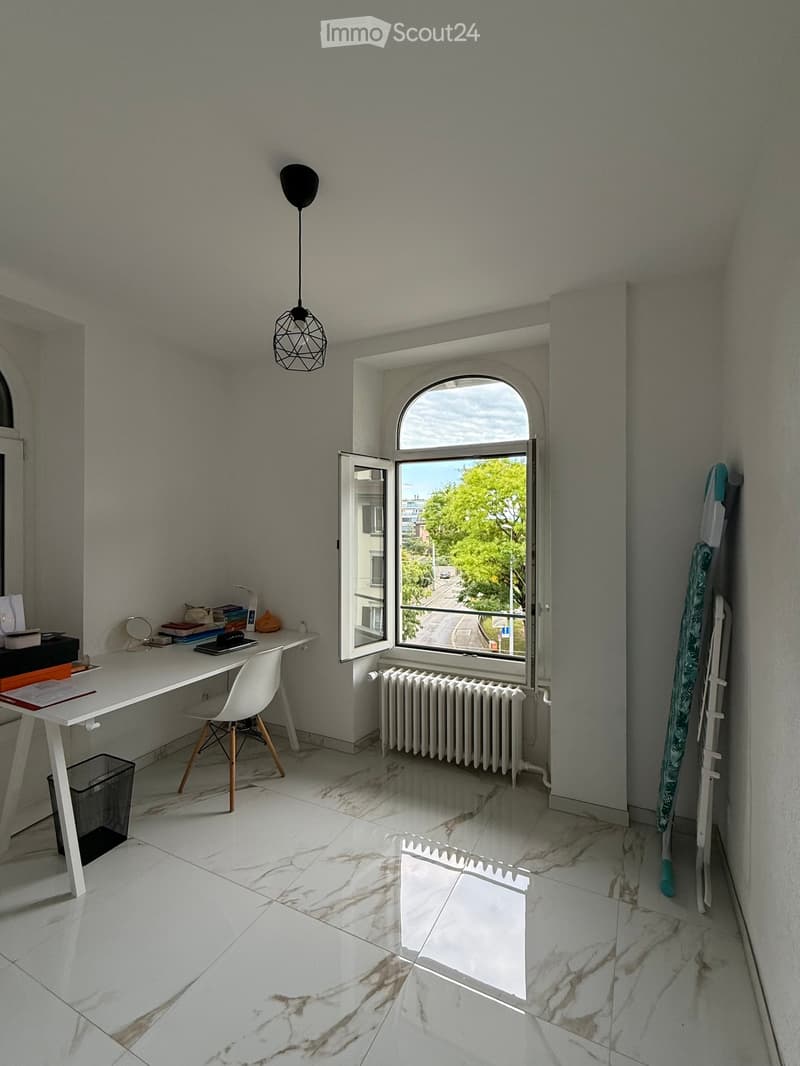 Modern, minimalist room with white marble flooring, a large arched window, a white desk with a chair, a hanging geometric lamp, and a radiator below the window.