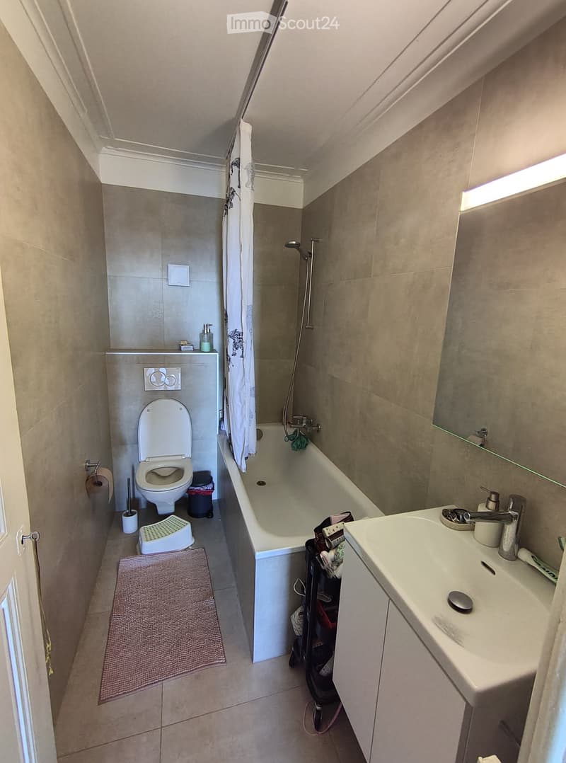 Compact bathroom with a toilet, bathtub, sink, and mirror. Includes a shower curtain, bathroom rug, soap dispenser, and a small stool.
