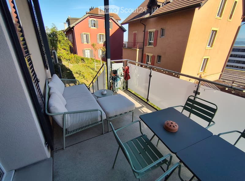 Balcony with a sofa, small table, and chairs, overlooking a hillside with neighboring houses.
