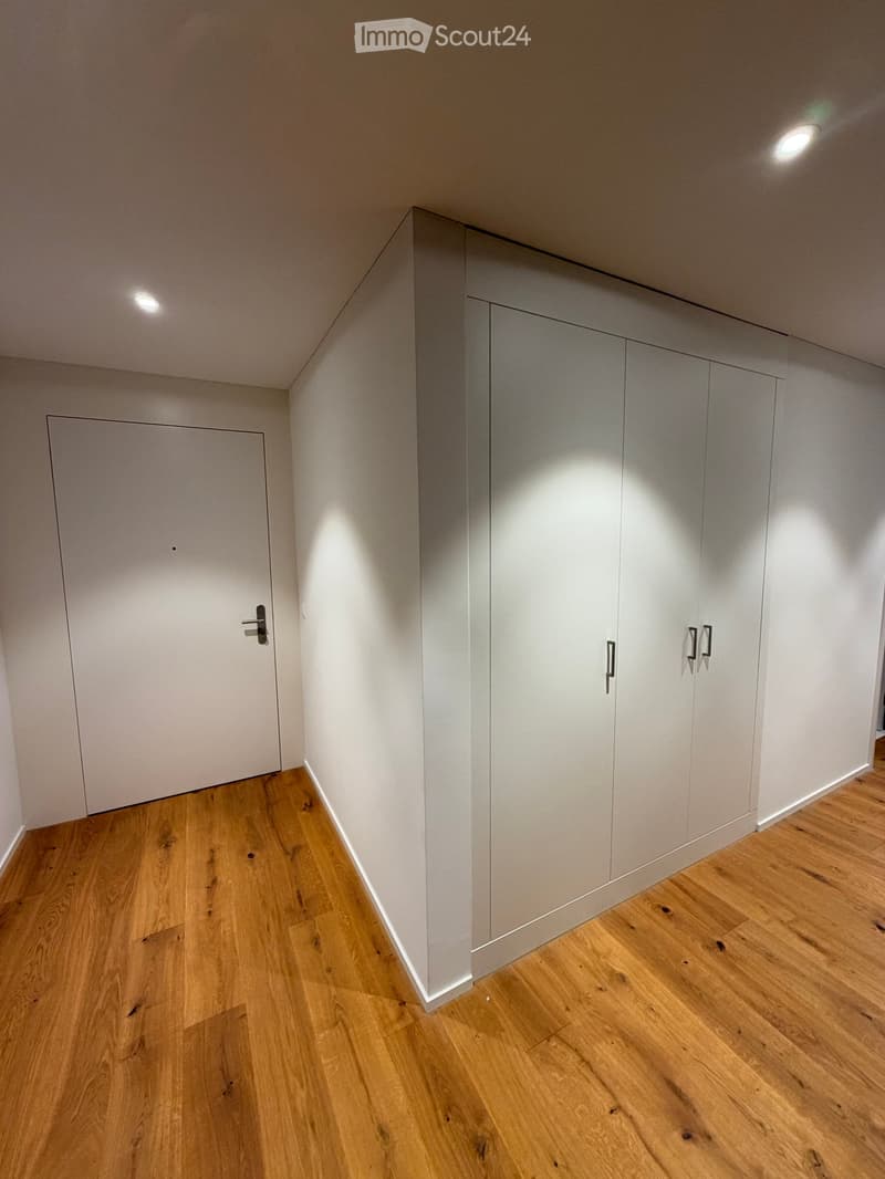 Empty room with light wooden flooring, white walls, built-in wardrobes, and a closed door.