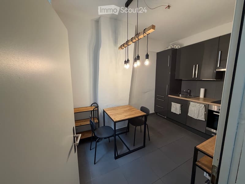 Modern kitchen with dark grey cabinets, a wooden dining table with chairs, and a hanging light fixture above the table.