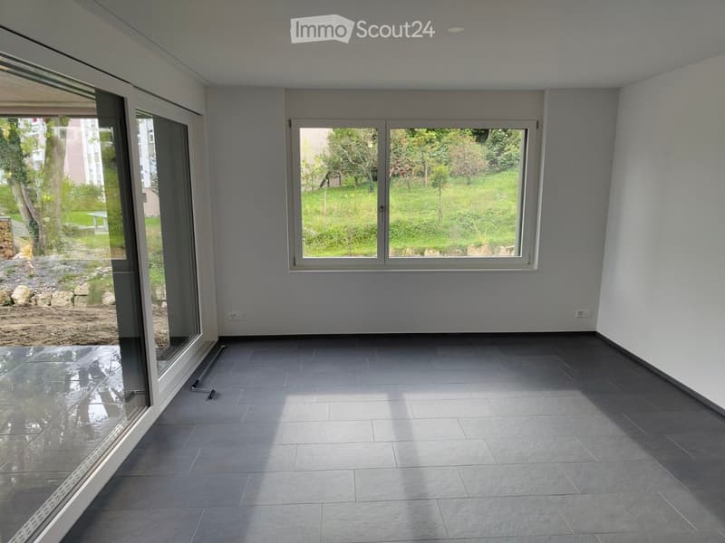 Empty room with grey tiled floor, large windows, and glass sliding doors leading to an outdoor area.
