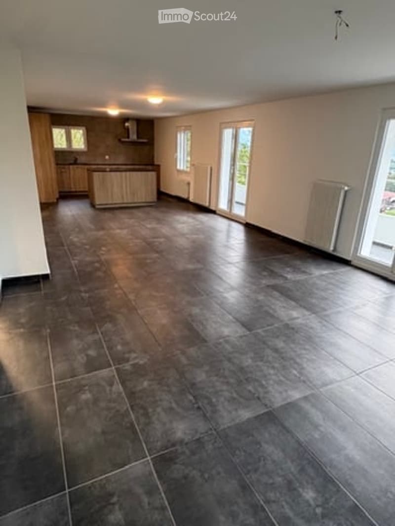 Empty room with dark grey tiled floor, white walls, and large windows with sliding doors leading to an outdoor area. The room is unfurnished, showing only the basic structure and flooring.