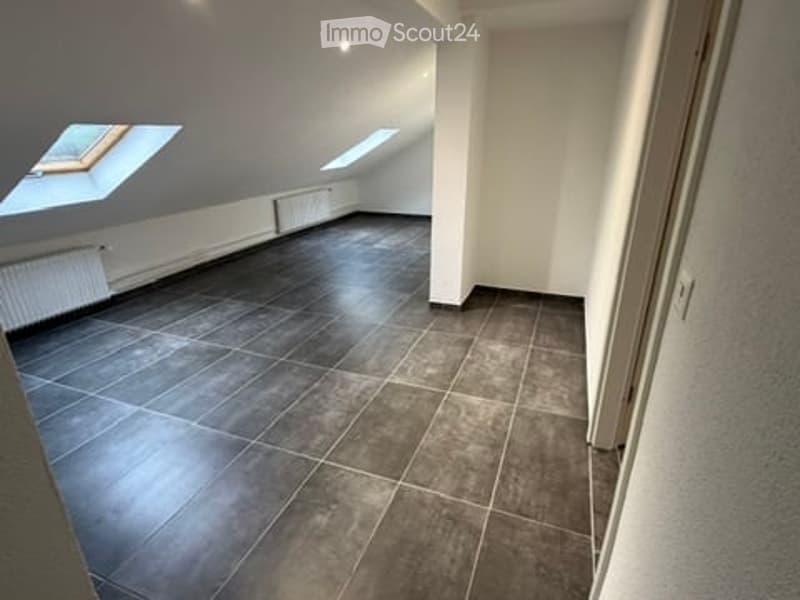 Empty attic room with dark tiled floor, white walls, and skylight windows.
