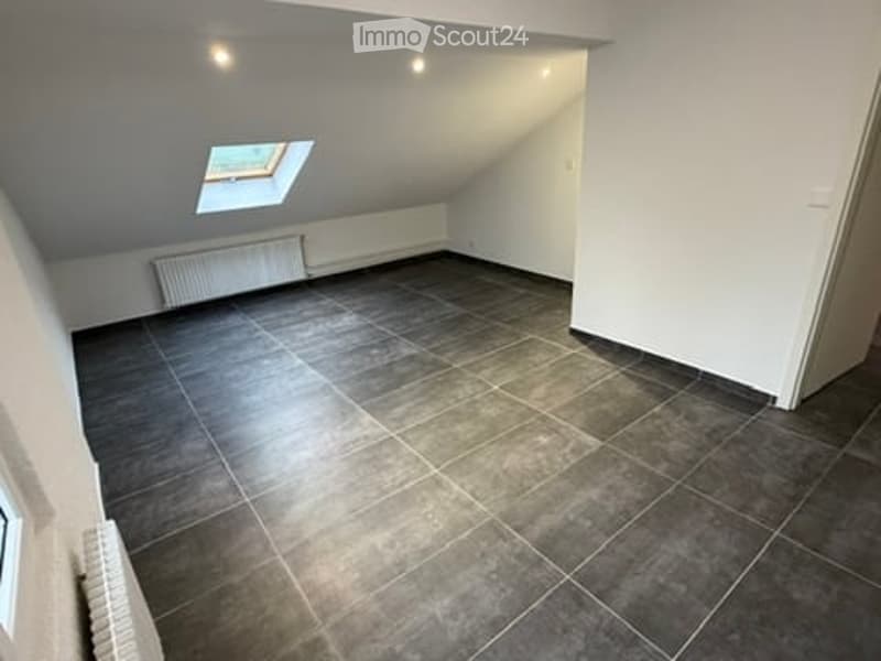 Empty attic room with dark tiled floor, white walls, and a skylight window. No furniture or equipment present.