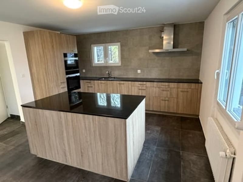 Modern kitchen with wooden cabinets, black countertop, island, built-in oven, and stainless steel range hood.