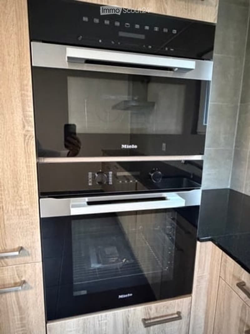 Modern kitchen with built-in microwave and oven, sleek black and silver design, wooden cabinetry.