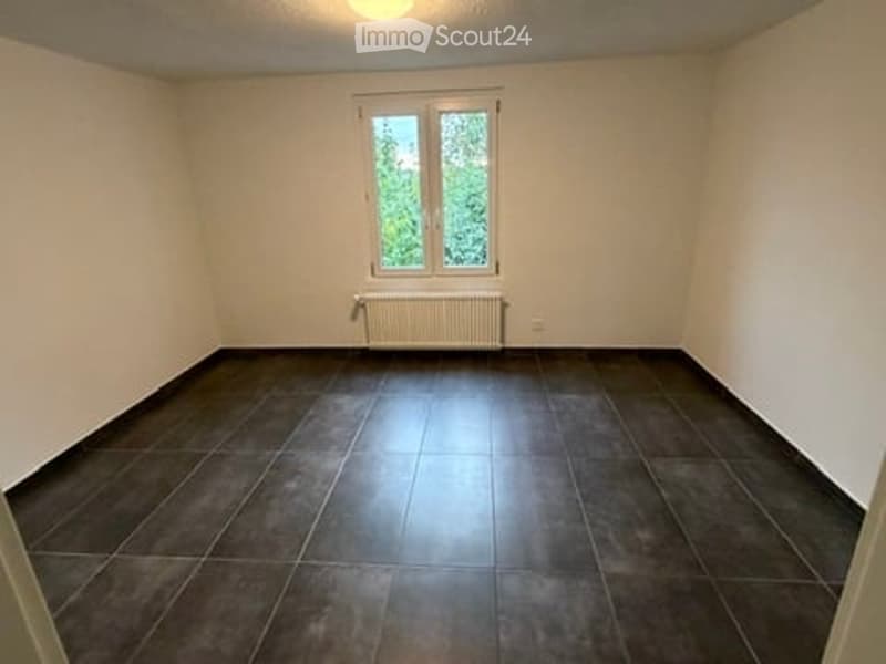 Empty room with dark tiled floor, white walls, and a single window with a radiator below it.