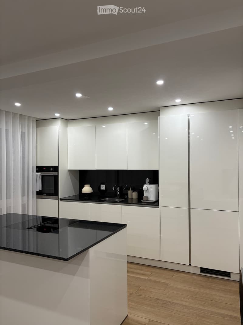 Modern kitchen with white cabinets, black countertops, and integrated appliances including an oven and coffee maker.