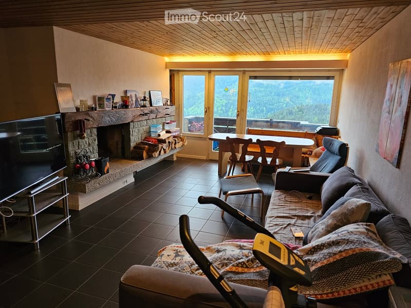 Cozy living room with a stone fireplace, large windows offering a scenic mountain view, a sofa, coffee table, chairs, and a dining table with chairs.