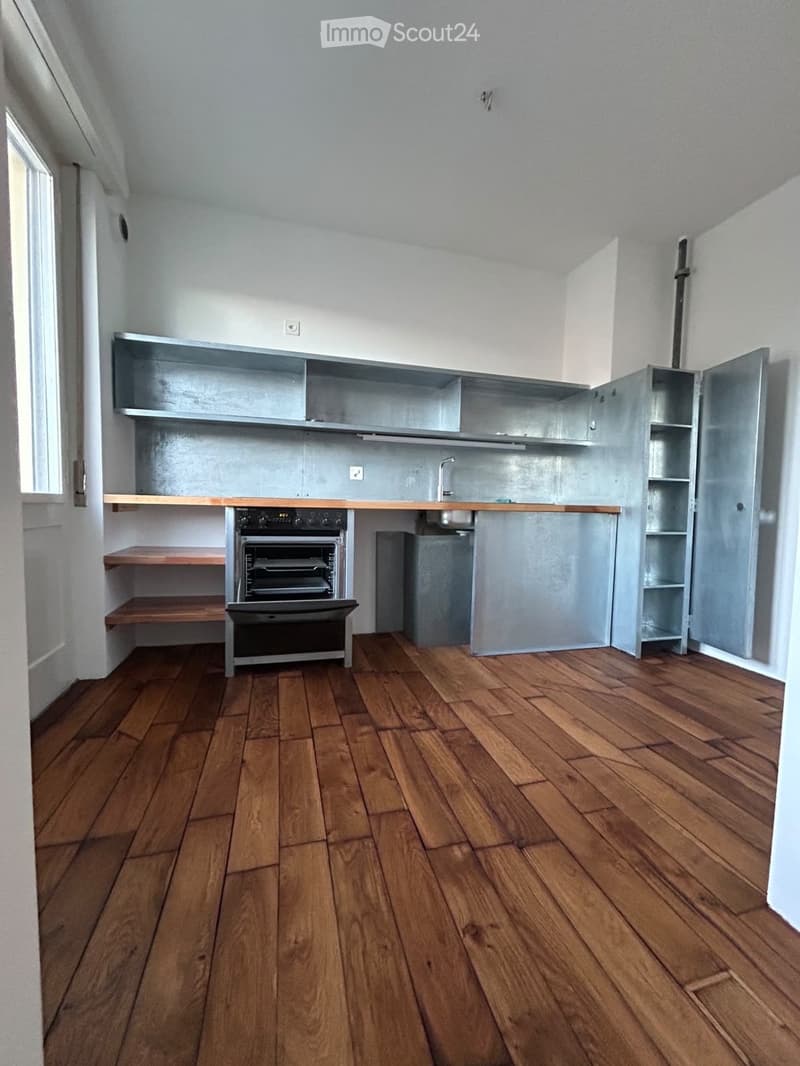 Modern kitchen with wooden flooring, stainless steel appliances, and open shelving.