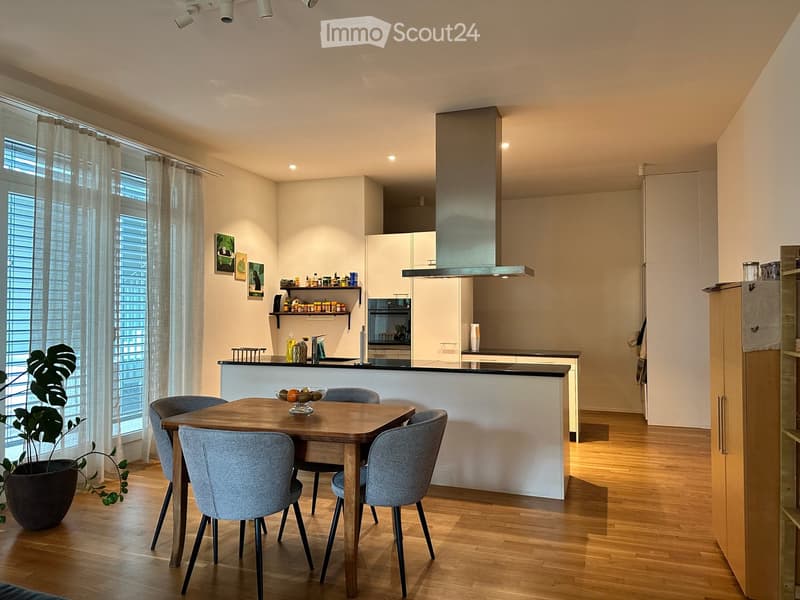 Modern kitchen and dining area with wooden flooring, white cabinets, stainless steel appliances, and a dining table with four chairs.