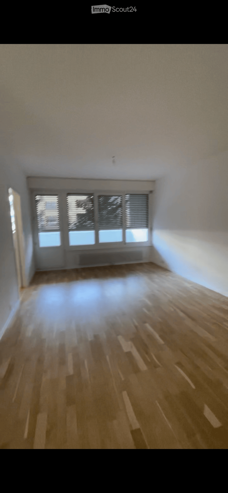 Empty room with wooden flooring, white walls, and large windows with blinds. No furniture or equipment present.