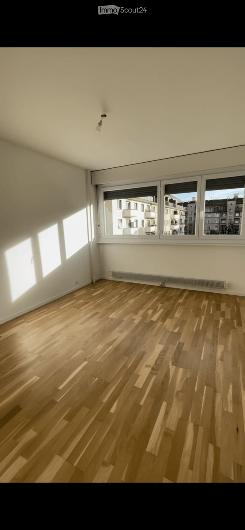 Empty room with wooden flooring, white walls, large windows, and a radiator. No furniture or equipment present.