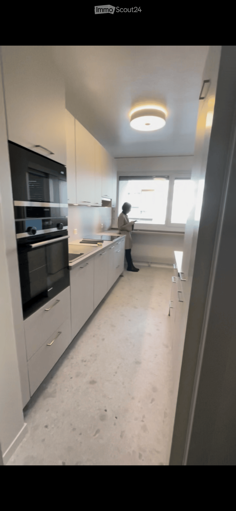 Modern kitchen with white cabinets, a built-in oven, and a sleek countertop, illuminated by a round ceiling light.