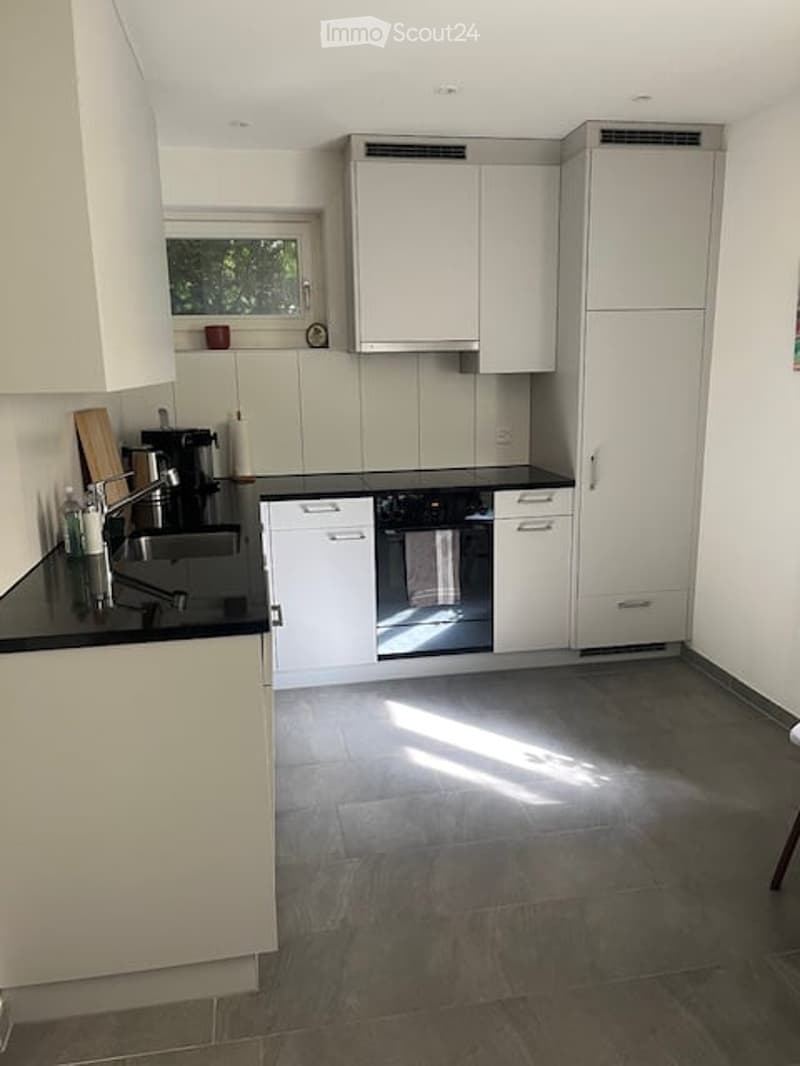 Modern kitchen with white cabinets, black countertops, and stainless steel appliances. Features a sink, faucet, oven, and coffee maker.