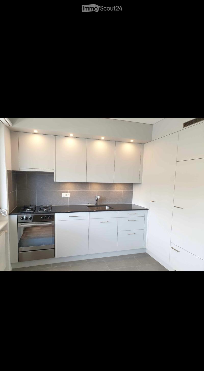Modern kitchen with white cabinets, stainless steel oven, sink, and faucet, featuring a black countertop and gray tiled floor.