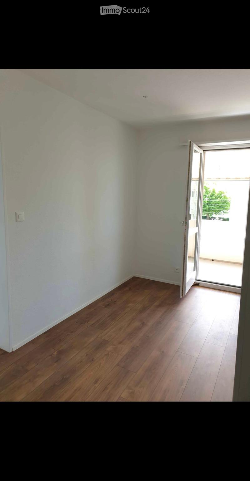 Empty room with wooden flooring and white walls, featuring an open sliding door leading to a balcony or outdoor area.