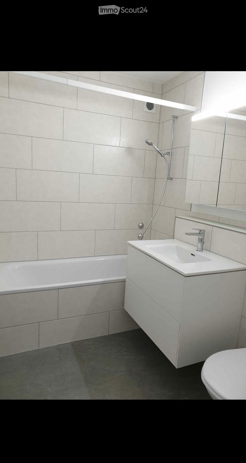 Modern bathroom with a bathtub, sink, toilet, and showerhead. Features light-colored tiles and a sleek design.