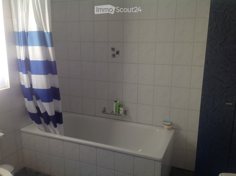 Bathroom with a bathtub, shower curtain, and a shelf holding various bottles and a cup.