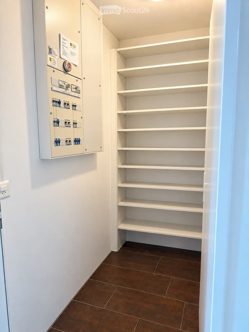 Empty storage closet with white built-in shelves and a brown tiled floor. Electrical panel visible on the left wall.