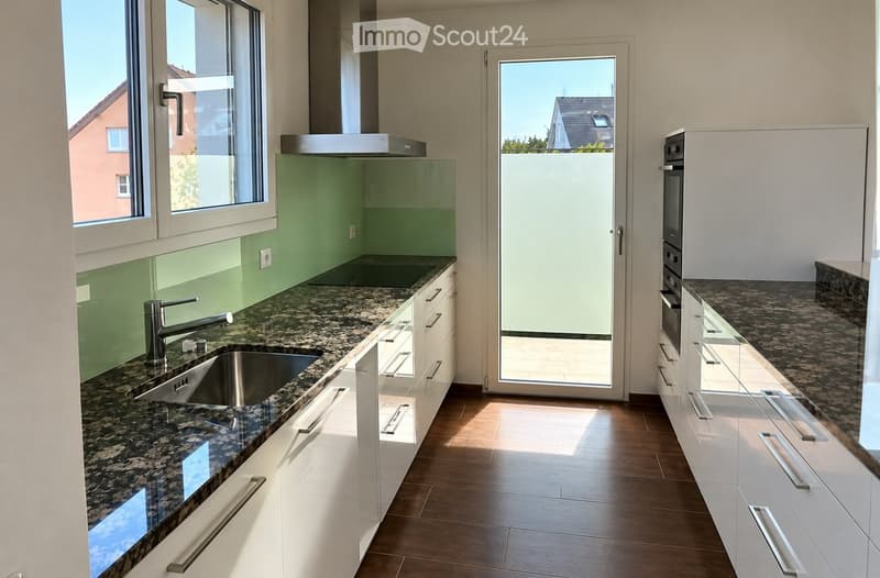 Modern kitchen with white cabinets, granite countertops, stainless steel sink and faucet, built-in oven, and a large window offering a view of the exterior.