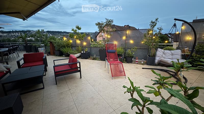 Balcony with tiled floor, red and black seating, wicker furniture, potted plants, and a scenic city view.