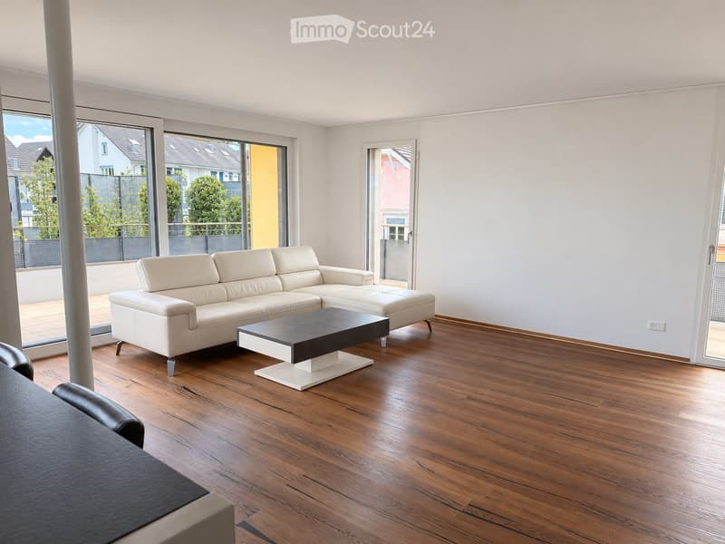 Modern living room with light-colored leather sofa, black coffee table, and large windows offering a view of the outdoor area.