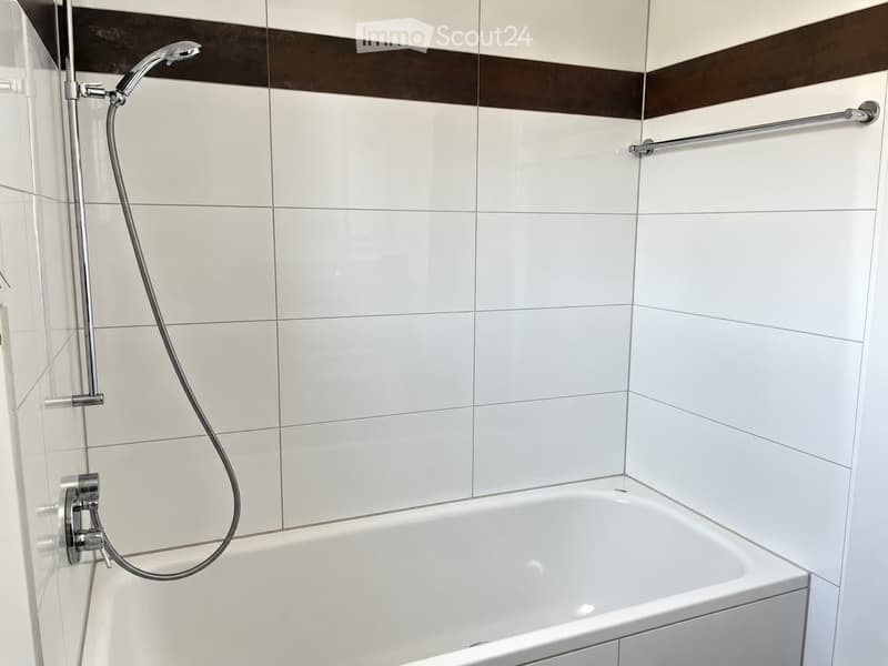 Modern bathroom with white tiled walls, a bathtub, a handheld showerhead, and a shower rail.