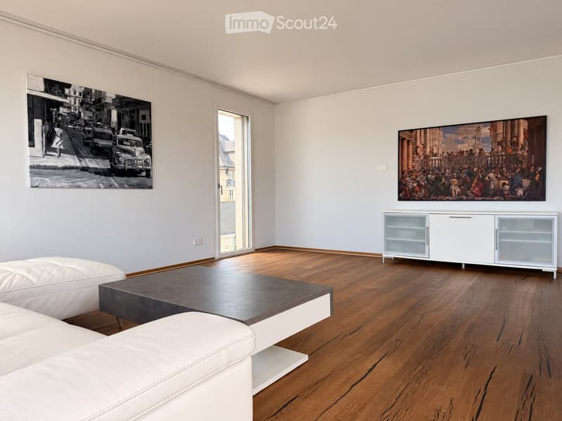 Modern living room with light grey walls, wooden flooring, white leather sofa, dark coffee table, and a white cabinet with glass doors.