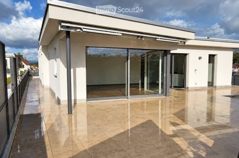 Modern rooftop terrace with large glass sliding doors, tiled flooring, and a sleek white building facade.