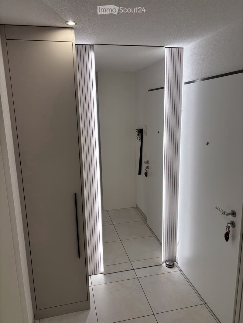 Modern hallway with tiled floor, white walls, and two doors on either side. Keys and a small round object are visible on the floor near the right door.