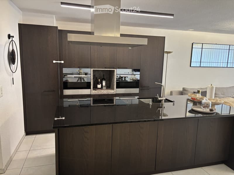 Modern kitchen with dark wood cabinets, black countertop, induction stove, oven, sink, and decorative items on the island.