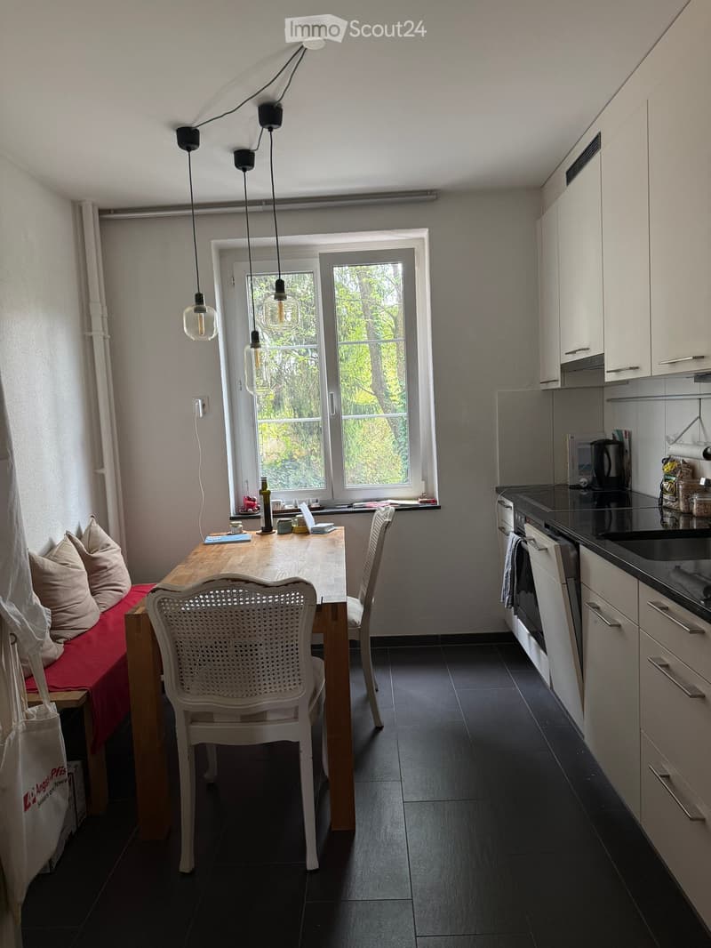 Modern kitchen and dining area with a wooden dining table, white chairs, a red bench, and modern kitchen cabinets with stainless steel appliances.