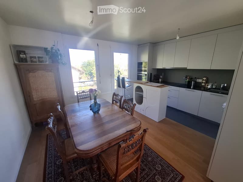 Bright dining area with wooden table and chairs, white cabinets, and a small kitchen area with appliances.
